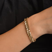 Gold bracelet on a wrist against a black background