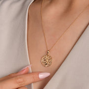 Model wearing large gold tree of life pendant with stone detail.