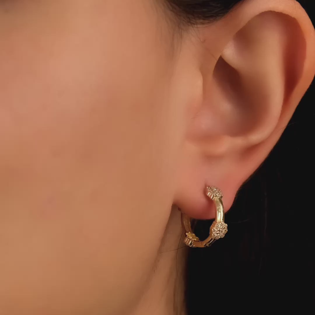 Close-up video of a woman's ear wearing 14ct solid gold hoop earrings adorned with flower-shaped cubic zirconia clusters.