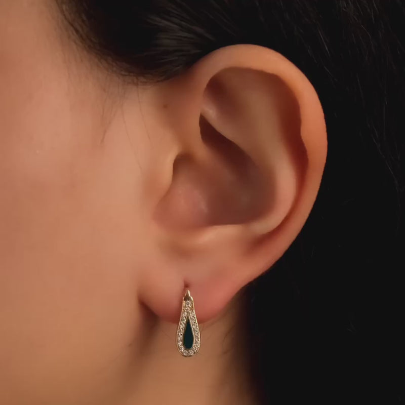 Close-up video of a model wearing solid gold teardrop earrings adorned with green enamel and surrounded by cubic zirconia stones, showcasing an elegant and stylish look.