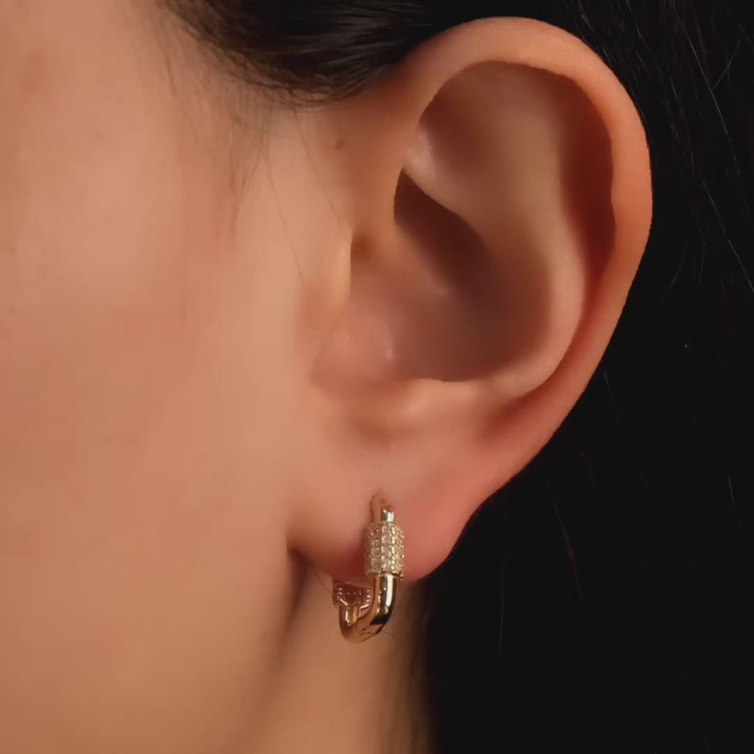 Close-up video of a woman's ear wearing 14ct solid gold hoop earrings with a rectangular cubic zirconia-encrusted segment.