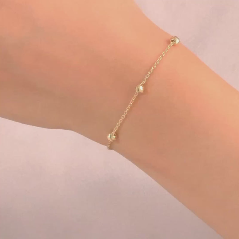 Close-up of the bracelet on a woman's wrist, highlighting the dainty gold beads and chain design.