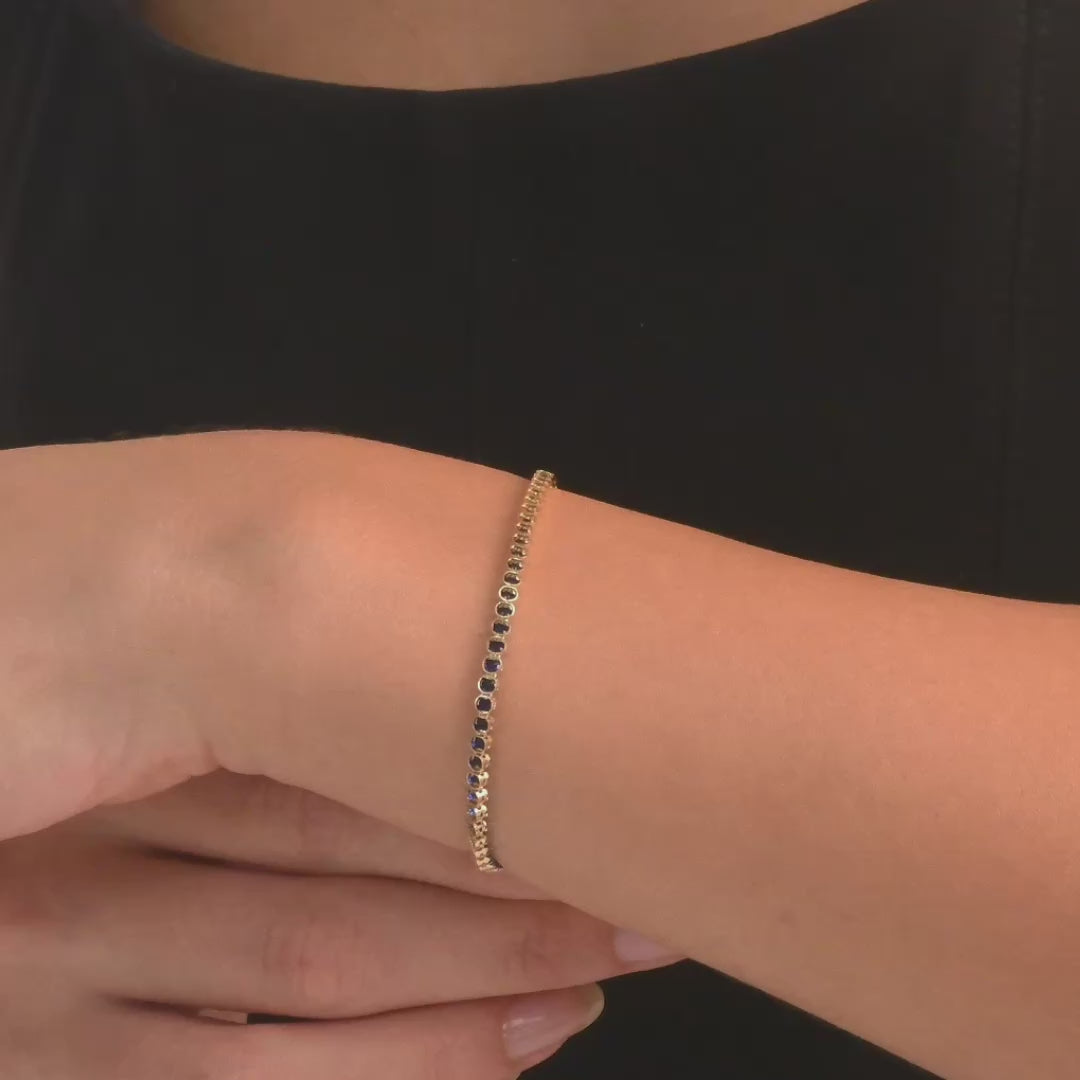 Video of woman in black dress, wearing the 14ct gold, sapphire blue gemstone tennis bracelet, showing its elegant design on her wrist.