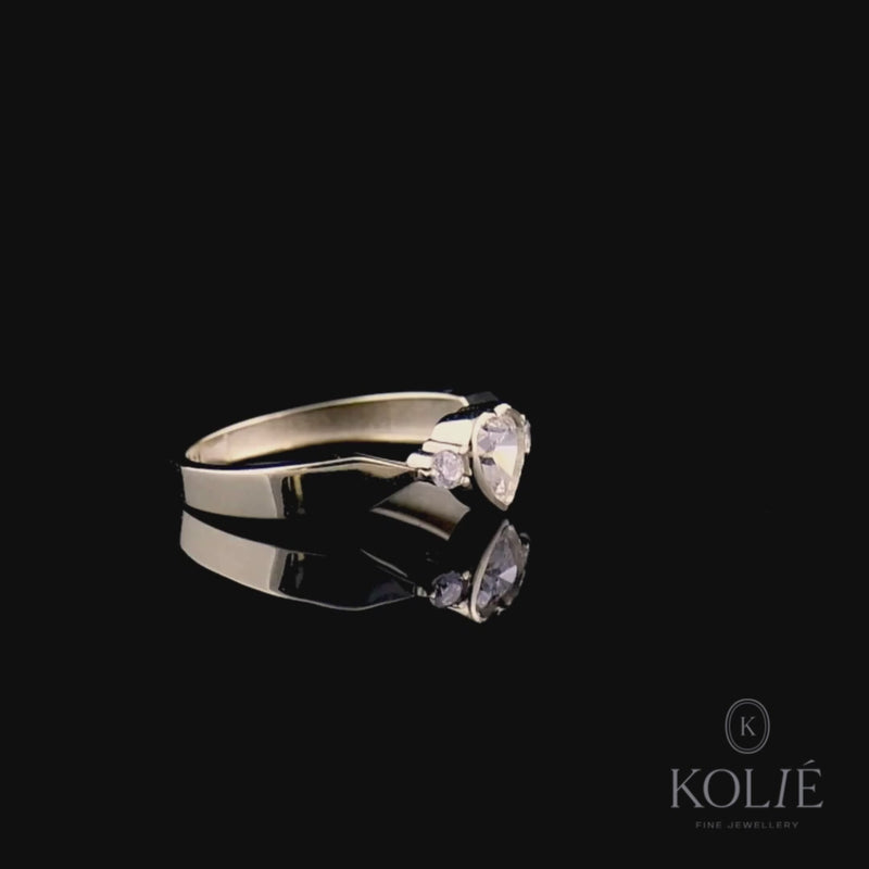 Kolié 9ct yellow gold ring featuring a heart-shaped cubic zirconia flanked by round brilliants on a satin-finish band.