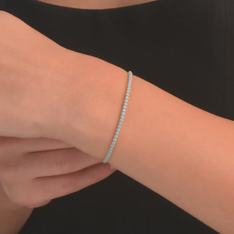 Woman wearing the 14ct gold bracelet with blue cubic zirconia, showcasing its elegant and colourful design.