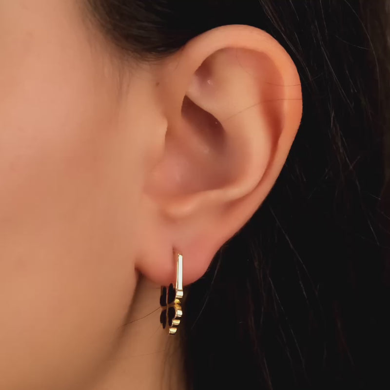 Close-up video of a woman's ear wearing 14ct solid gold clover-shaped hoop earrings with black enamel accents.