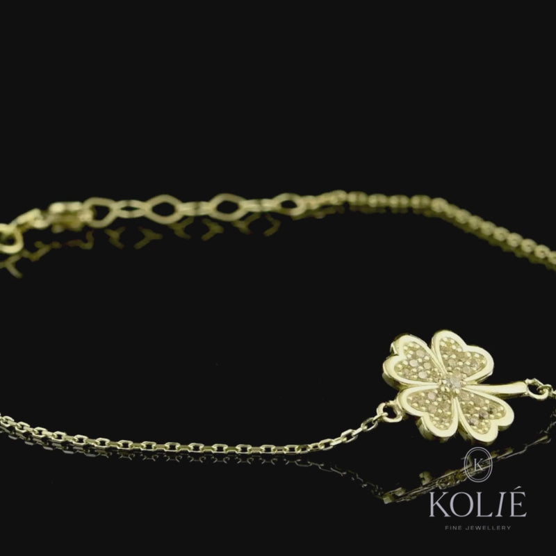 Elegant 9ct yellow gold bracelet with a sparkling four-leaf clover charm set with zirconia, symbolizing luck and fortune, on a fine gold chain, against a black background, from Kolié's signature collection.