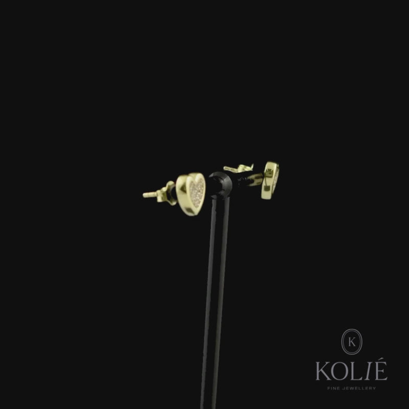 Kolié 9ct yellow gold heart-shaped stud earrings, filled with sparkling zirconia, offering a glimpse of love's radiance against a black background. Find these enchanting earrings at www.kolie.co.uk