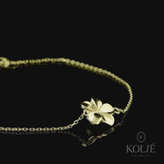 Elegant Kolié 9ct yellow gold bracelet featuring a simple yet sophisticated floral charm, a design that captures the essence of nature, set against a contrasting black backdrop. Available at www.kolie.co.uk.