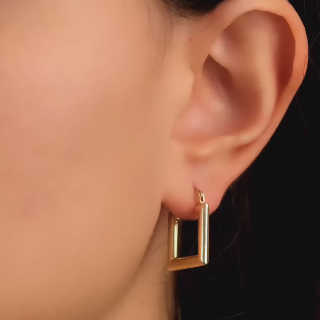 Close-up video of a model wearing solid gold rectangular earrings with a smooth and shiny surface, adding a touch of sophistication and style to her look.